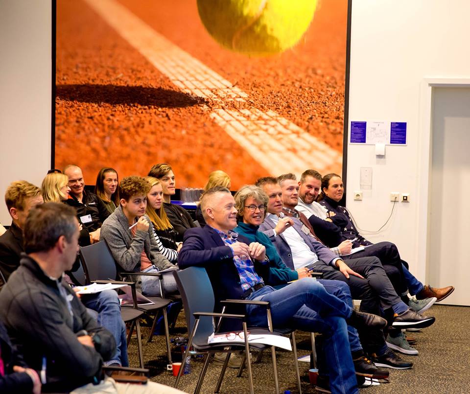 In zaaltje met andere deelnemers met tennisbal op muur achtergrond